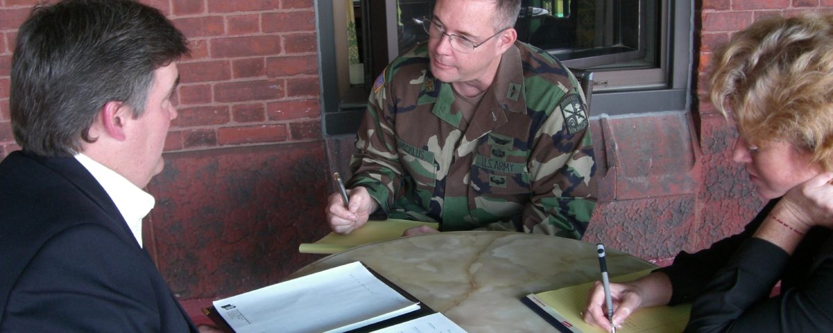 Military officer discussing documents with two men at a round table.